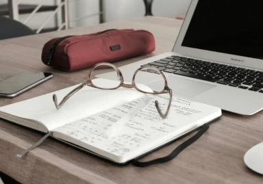 Glasses on an open notebook next to the laptop