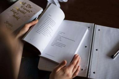 A person holding an open book on the background of a workbook